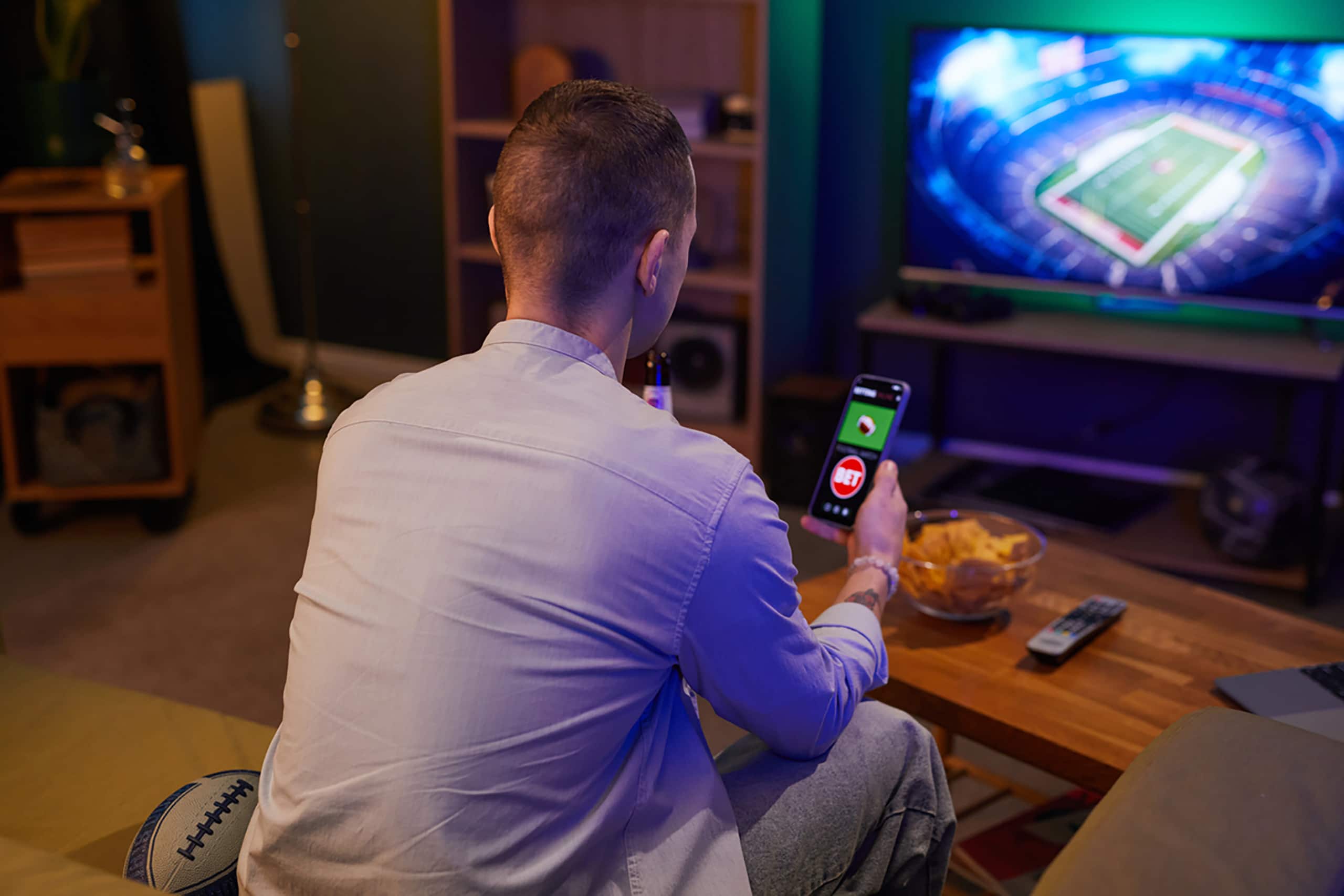 Person sitting on couch while using sports betting app on smartphone at home